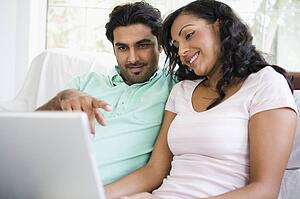 Couple in living room with laptop pointing and smiling (high key/selective focus)