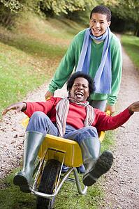 Young boy outdoors pushing mother in wheelbarrow and smiling (selective focus)