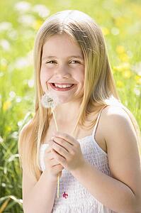 Young girl sitting outdoors holding dandelion head smiling