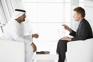 Two businessmen indoors with a laptop talking and smiling (high key/selective focus)