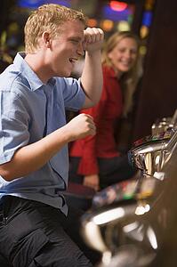 Man in casino playing slot machine smiling with people in background (selective focus)