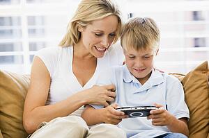 Woman and young boy in living room with handheld video game smiling