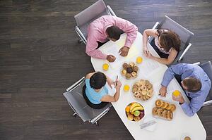Four businesspeople at boardroom table with breakfast