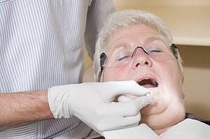 Dentist in exam room fitting dentures on woman in chair