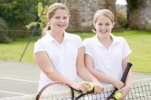 Two young girl friends with rackets on tennis court smiling