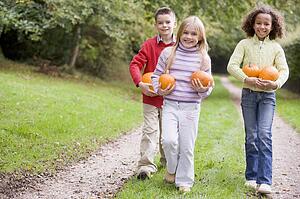 Three young friends walking on path with pumpkins smiling