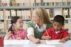 Two students in class writing with teacher helping