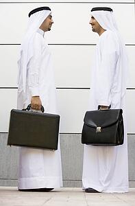 Two businessmen standing outdoors with briefcases smiling