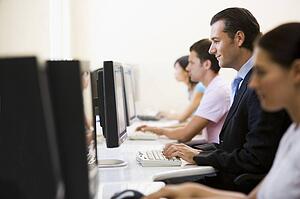 Four people sitting in computer room typing with one man in a suit