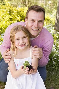 Father and daughter outdoors holding plant smiling