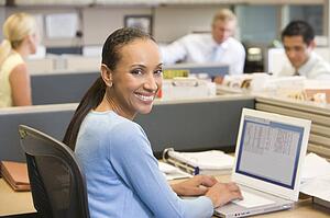 Businesswoman in cubicle using laptop smiling