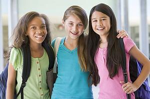 Three students standing outside school together smiling (selective focus)
