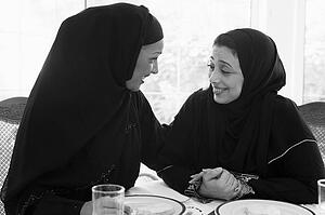 Two women sitting at dinner table smiling (high key)