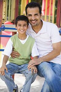 Father and son sitting on playground structure smiling (selective focus)