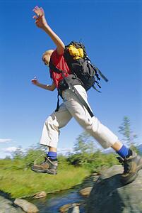 Woman hiking outdoors jumping over stream (blur)