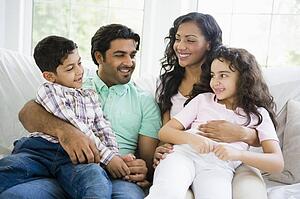 Family in living room sitting on sofa smiling (high key)