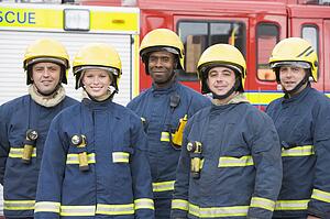 Five firefighters standing by fire engine wearing helmets