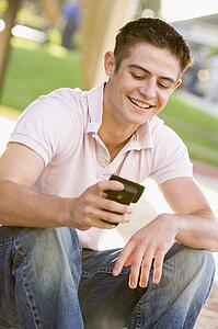 Teenage Boy Sitting Outdoors Using Mobile Phone