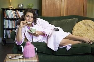 Young woman lying on sofa at home eating cookies and drinking tea