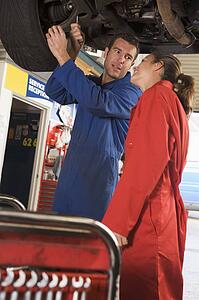 Two mechanics working under car smiling