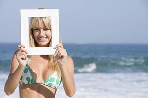 Woman on a beach holding a frame to her face