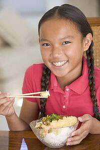Young girl in dining room eating Chinese food smiling