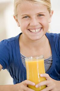 Young girl indoors drinking orange juice smiling
