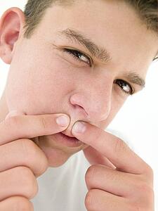 Teenage boy popping zit on face
