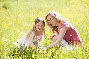 Mother and daughter outdoors holding flower smiling