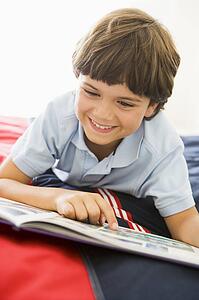 Young Boy Lying Down On His Bed Reading A Book
