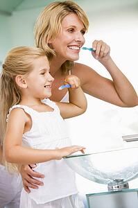 Woman and young girl in bathroom brushing teeth