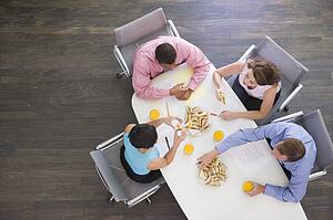Four businesspeople at boardroom table with sandwiches