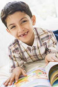 Young boy in living room reading a book and smiling (high key)