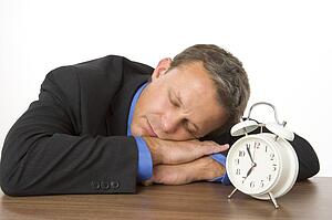 Businessman Asleep On Desk By An Alarm Clock 