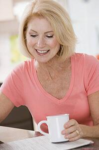 Woman in kitchen with coffee and newspaper smiling
