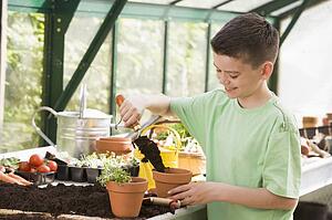 Young boy in greenhouse putting soil in pot smiling