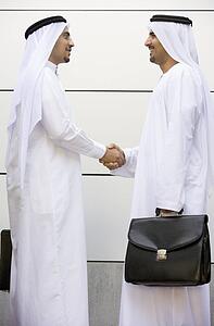 Two businessmen outdoors shaking hands and smiling