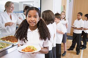 Students in cafeteria line with one holding her healthy meal and looking at camera (depth of field)
