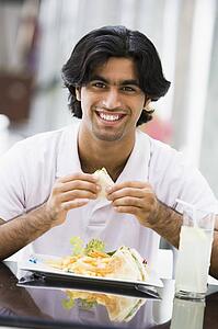 Man at restaurant eating sandwich and smiling (selective focus)