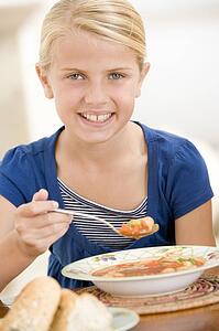 Young girl indoors eating soup smiling