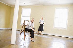 Two women with ladder in empty space holding paper smiling