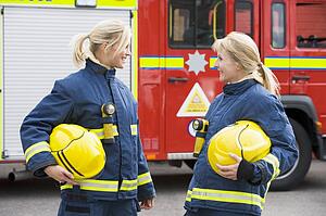 Two firewomen standing by fire engine talking