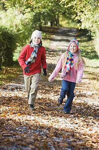 Two young children running outdoors in park and smiling