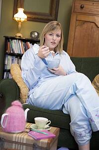 Young woman lying on sofa at home eating a sweet treat