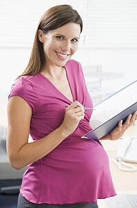 Pregnant woman at work writing in binder smiling