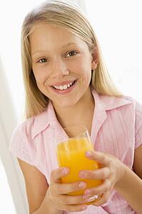 Young girl indoors drinking orange juice smiling