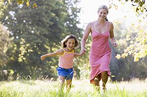 Woman and young girl running outdoors holding hands and smiling