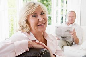 Woman in living room smiling with man in background reading newspaper