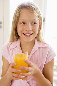 Young girl indoors drinking orange juice smiling