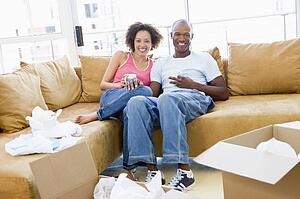 Couple relaxing with coffee by boxes in new home smiling